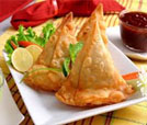 Three crispy samosas on a plate next to a glass of juice, showcasing the flavors of Indian and Nepali culinary traditions.