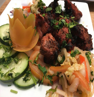 A beautifully arranged plate with succulent meat, vibrant vegetables, and crisp cucumbers, highlighting Indian and Nepali cuisine.