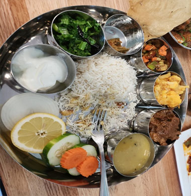 A beautifully arranged plate of Indian and Nepali dishes next to a silver bowl, exemplifying top-tier catering services.