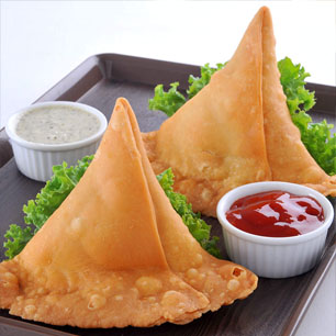 Two crispy samosas on a plate with a bowl of flavorful sauce, representing the best of Indian and Nepali culinary traditions.